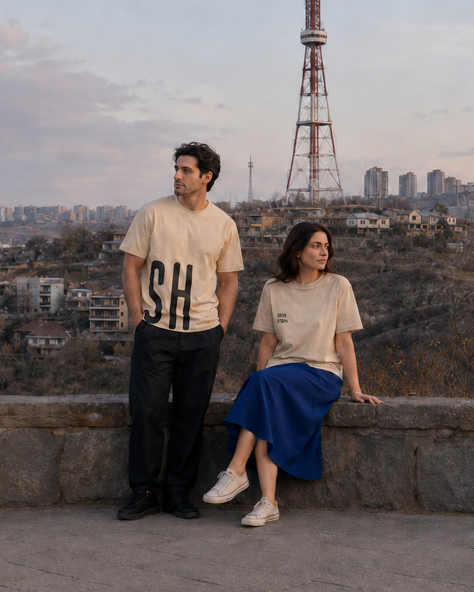 Two models wearing beige URISH T-shirts with the Yerevan skyline and television tower behind them